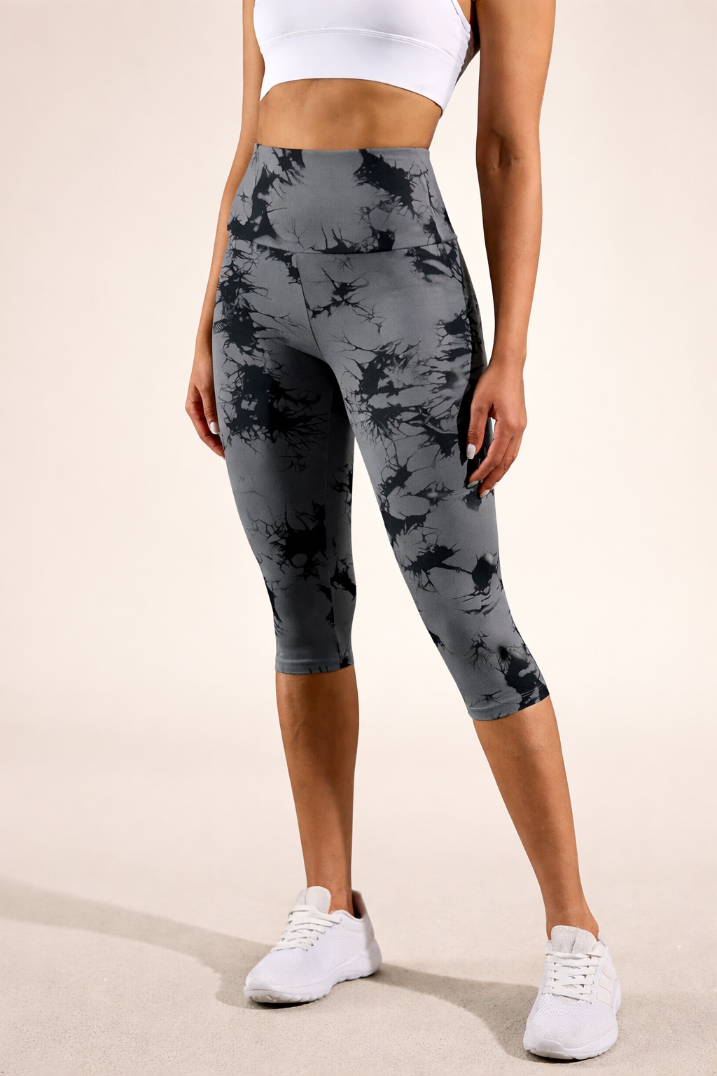 Person wearing gray camouflage leggings with a white top and sneakers on a beige background