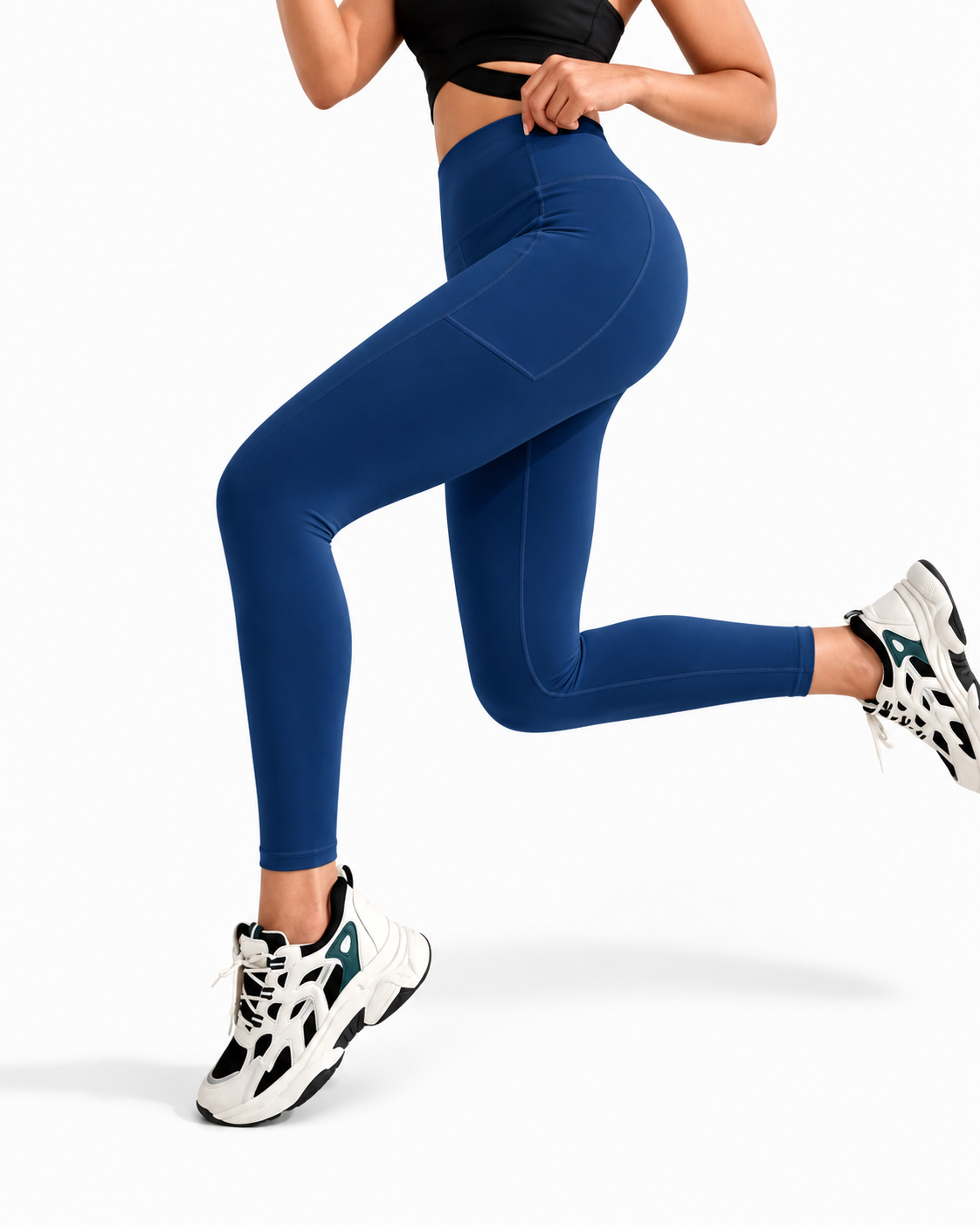 A person wearing high-waisted blue leggings and white sneakers with black and green accents, captured mid-stride against a clean white studio background.
