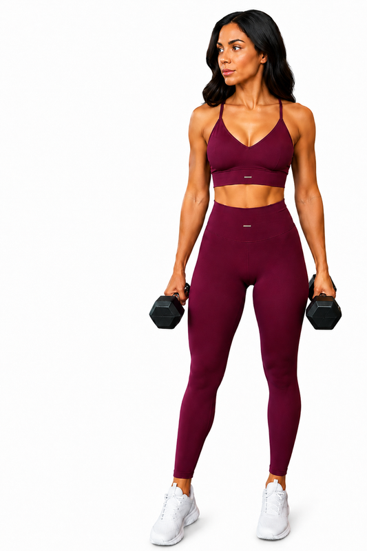 Athletic model wearing the Fierce Ember™ Signature Training Set in deep burgundy, featuring a matching sports bra and high-waisted leggings while holding dumbbells against a clean white studio background.