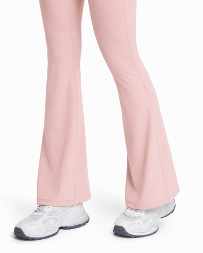 A close-up of a person's legs wearing light pink flared leggings and white athletic sneakers against a plain white background.