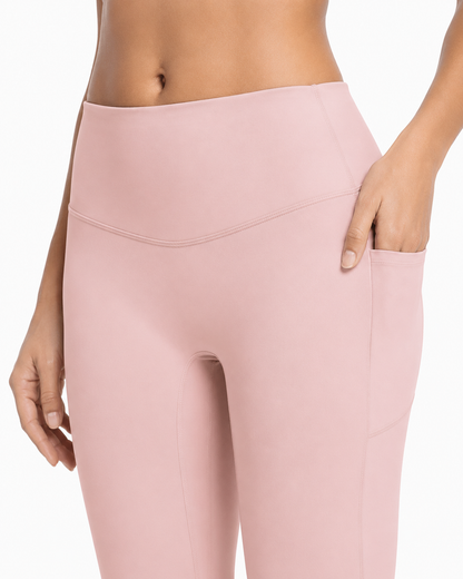A close-up of a model wearing high-waisted dusty pink leggings with a side pocket, shown from the waist down against a plain white background.