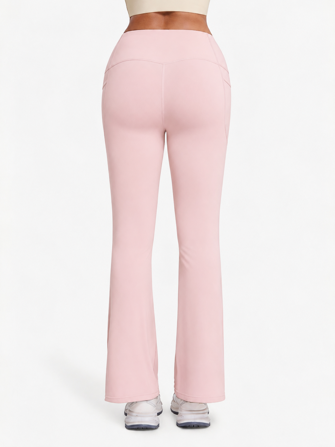 A person shown from the back wearing light pink high-waisted flared leggings or yoga pants, with a white crop top and white sneakers visible against a plain light background.