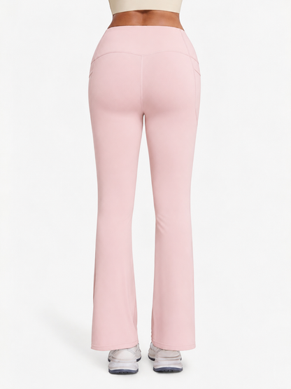 A person shown from the back wearing light pink high-waisted flared leggings or yoga pants, with a white crop top and white sneakers visible against a plain light background.