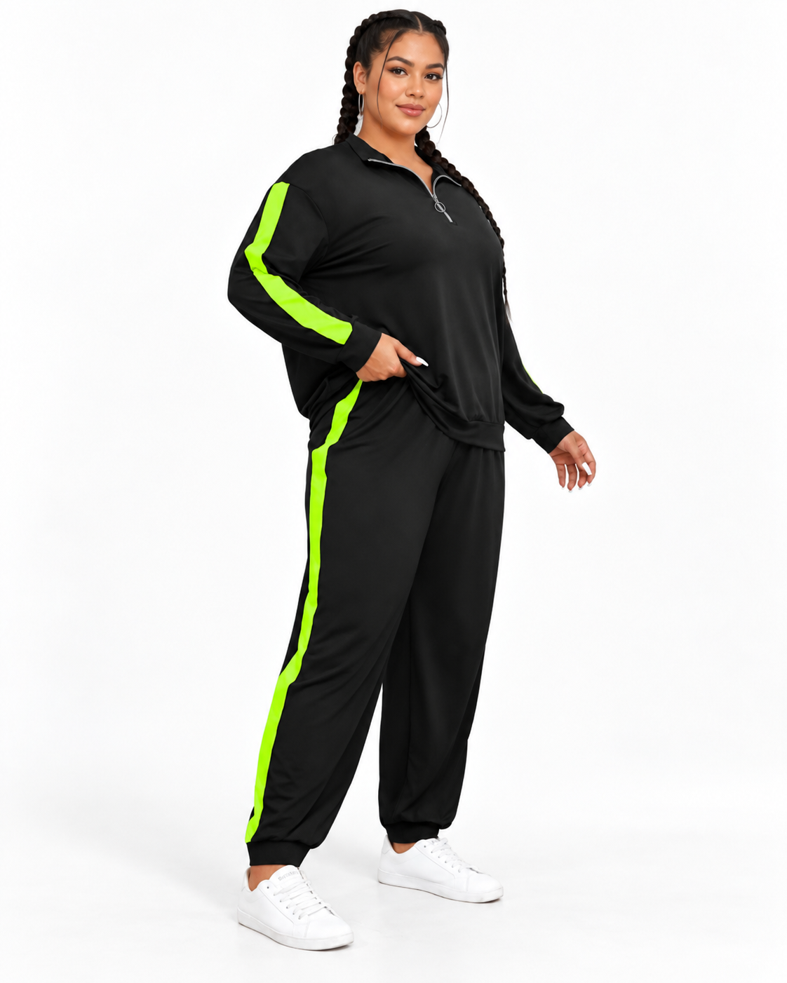 A woman modeling a black two-piece tracksuit with bright neon green side stripes, featuring a half-zip long-sleeve top and matching jogger pants, paired with white sneakers on a white studio background.