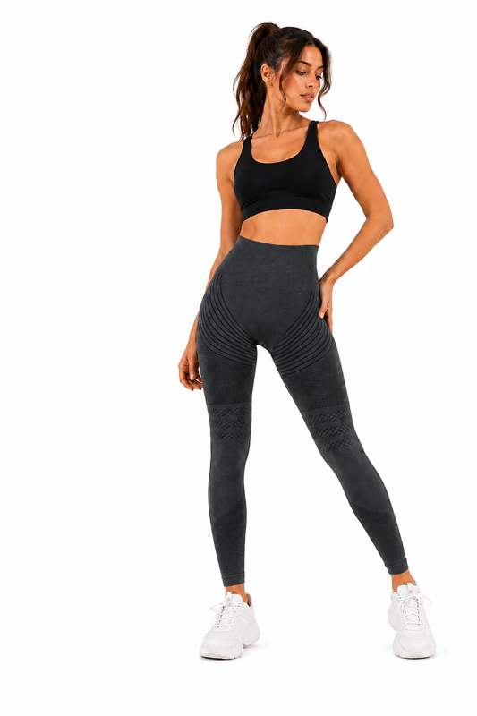 Full-length studio image of a woman wearing a black sports bra, charcoal grey seamless sculpting leggings and white trainers against a plain white background. The fitted activewear features ribbed contour detailing and a high-waisted design, creating a sleek, supportive silhouette ideal for gym training, fitness and everyday activewear