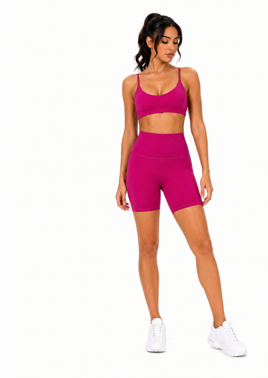 Athletic woman wearing the Power Vibe™ Signature Training Set in Electric Pink, featuring a matching sports bra and high-waisted biker shorts on a clean white studio background.