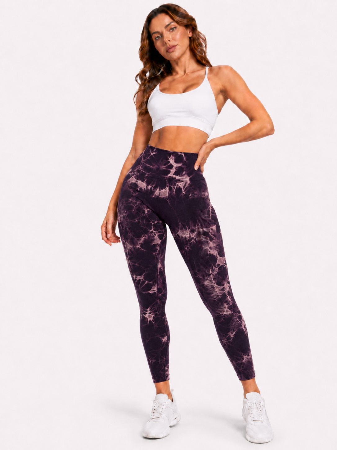 Woman modelling purple and white marble-pattern high-waisted leggings with a white sports bra and white trainers on a plain white background.