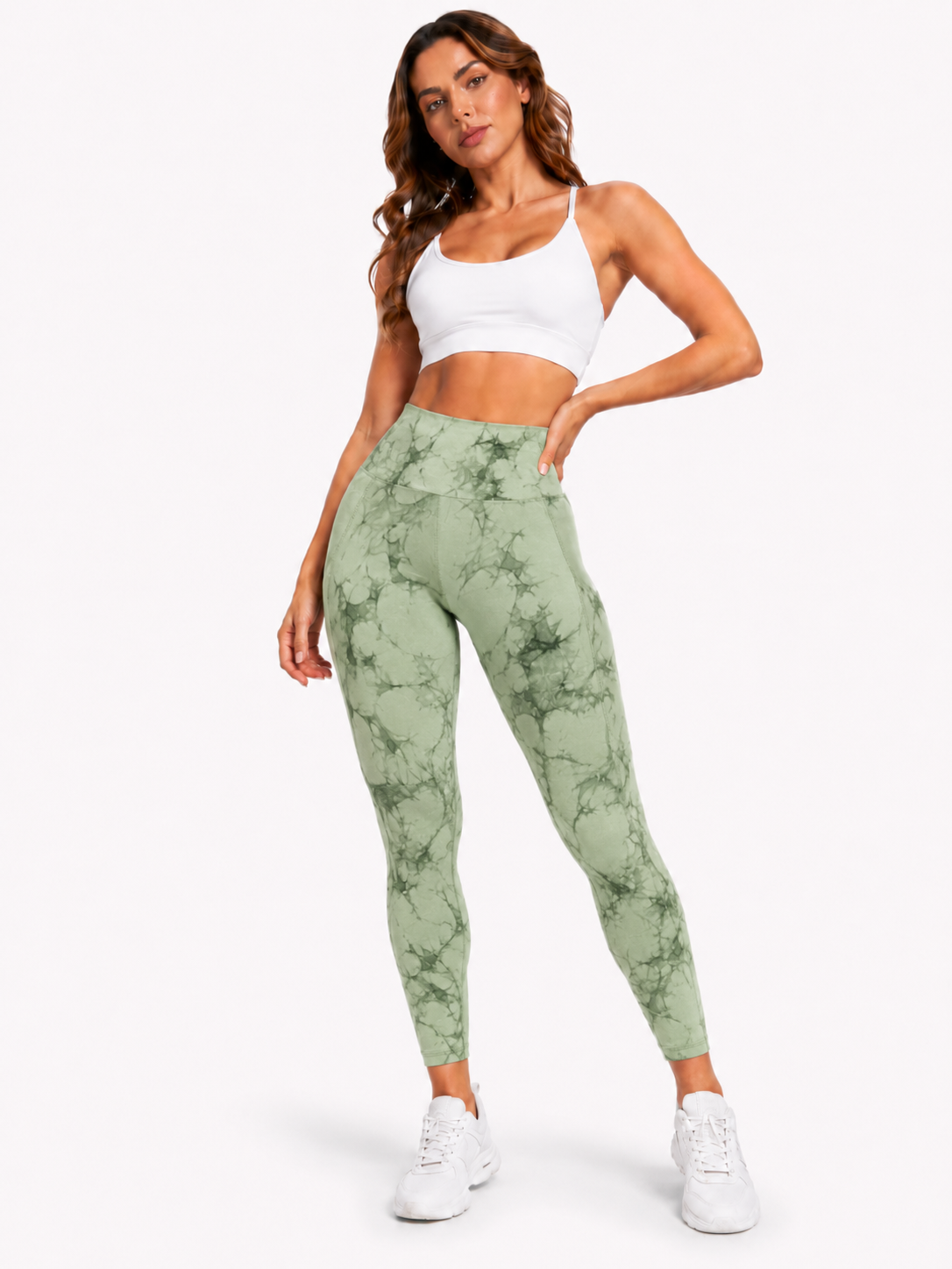 Woman modelling light green and dark green marble-pattern high-waisted leggings with a white sports bra and white trainers on a plain white background.