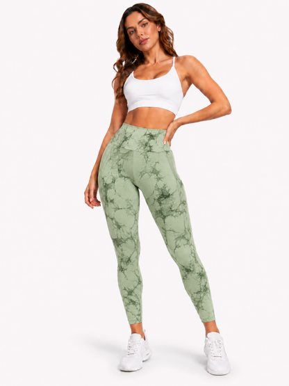 Woman modelling light green and dark green marble-pattern high-waisted leggings with a white sports bra and white trainers on a plain white background.