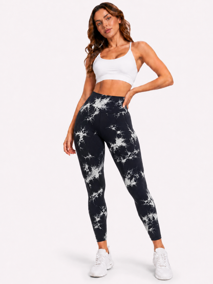 Woman modelling black and white marble-pattern high-waisted leggings with a white sports bra and white trainers on a plain white background.